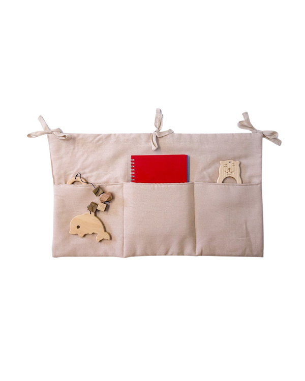 Pale pink linen toy organizer with three pockets hanging on a baby crib