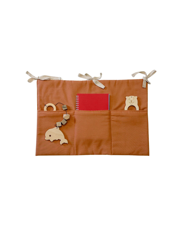 Terracotta linen crib organizer with three pockets tied to a baby crib